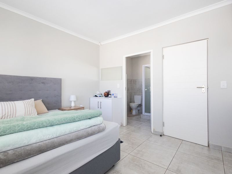 A well-maintained bedroom featuring neutral wall tones, tiled flooring, and direct access to an en-suite bathroom.