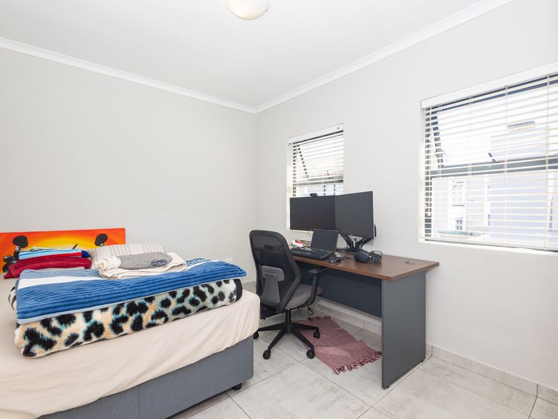 A functional bedroom featuring tiled flooring, neutral wall finishes, and dual windows fitted with venetian blinds, providing ample natural light.