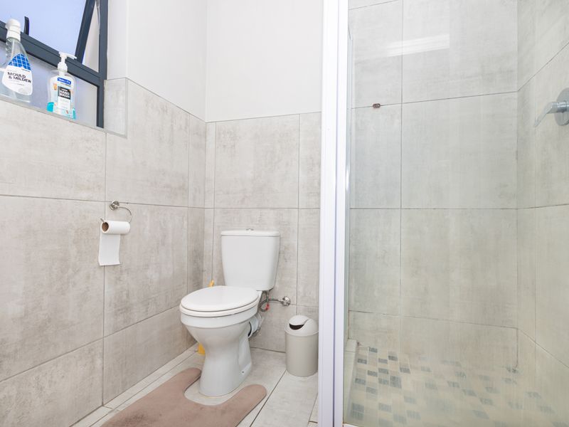A functional bathroom featuring a toilet and a glass-enclosed shower with neutral wall and floor tiling.