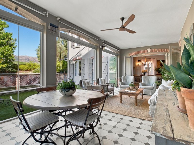 A spacious covered patio featuring elegant patterned floor tiles, a ceiling fan, and large glass stackable doors that open to the garden.