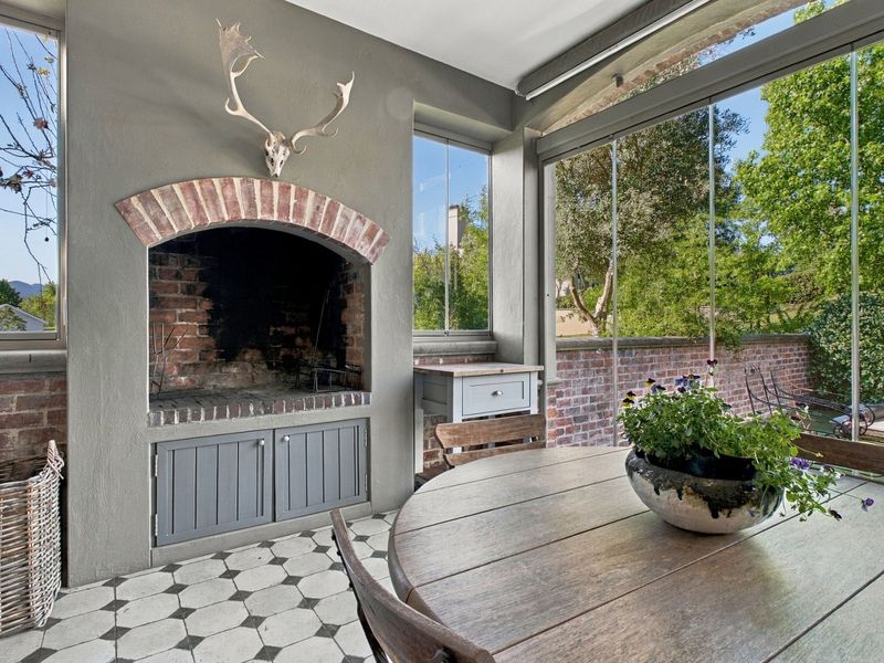 Enclosed patio area featuring a built-in brick fireplace, decorative arch, and glass paneling overlooking the garden.