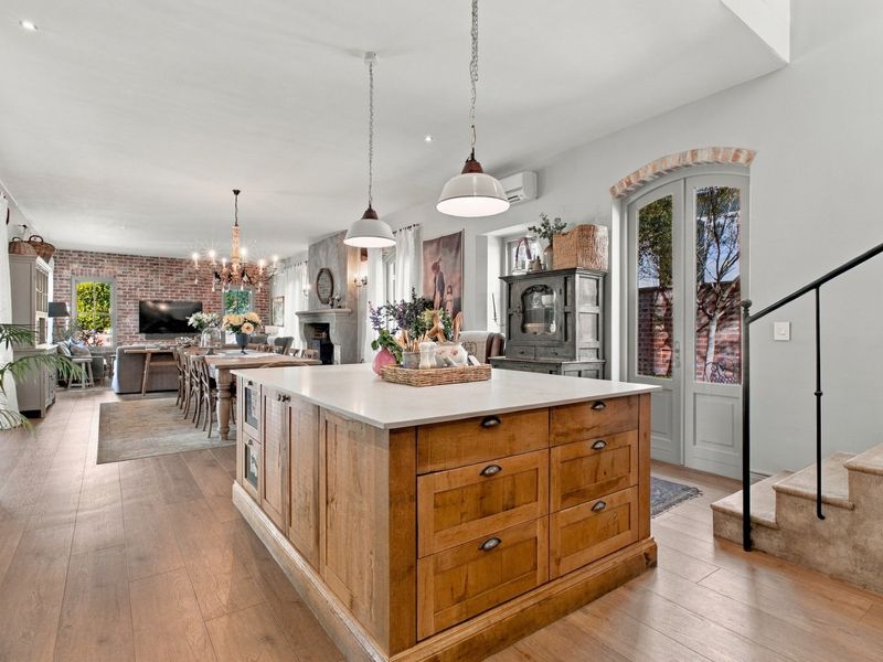 Spacious open-plan living area featuring a large wooden kitchen island, exposed brick accents, a fireplace, and elegant stone staircase leading to the upper level.