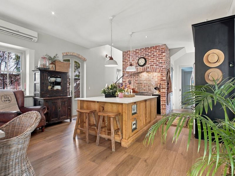 A charming kitchen featuring a central island, exposed brick chimney breast, and modern split system air conditioning, finished with warm wood-look flooring.