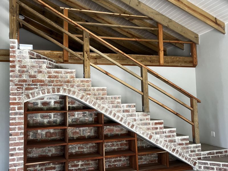 A bright living area featuring a unique brick staircase with integrated timber shelving, exposed wooden rafters, and polished concrete flooring.