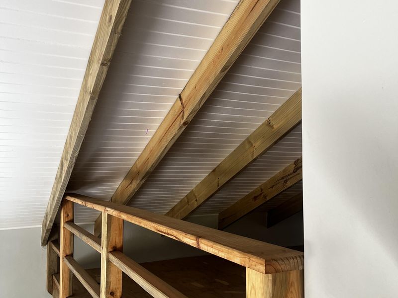 A mezzanine level featuring exposed timber rafters, a wooden balustrade, and tongue and groove ceiling finishes, suitable for storage or additional utility space.
