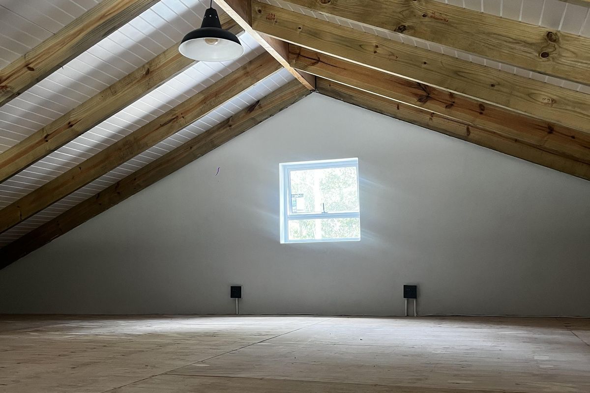 An attic-style bedroom featuring exposed timber rafters, a vaulted tongue and groove ceiling, and a single window, providing a bright and versatile living space.