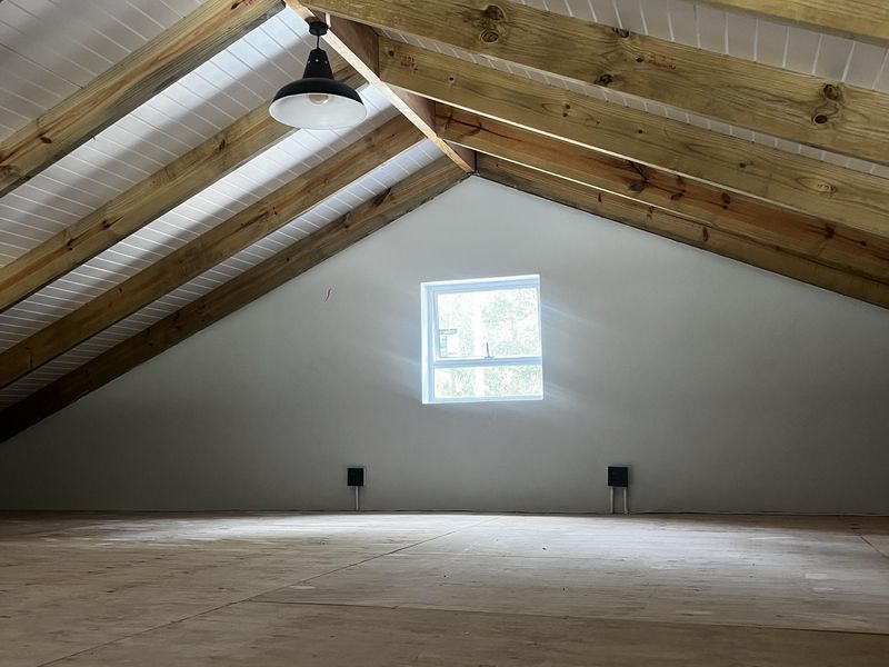 An attic-style bedroom featuring exposed timber rafters, a vaulted tongue and groove ceiling, and a single window, providing a bright and versatile living space.