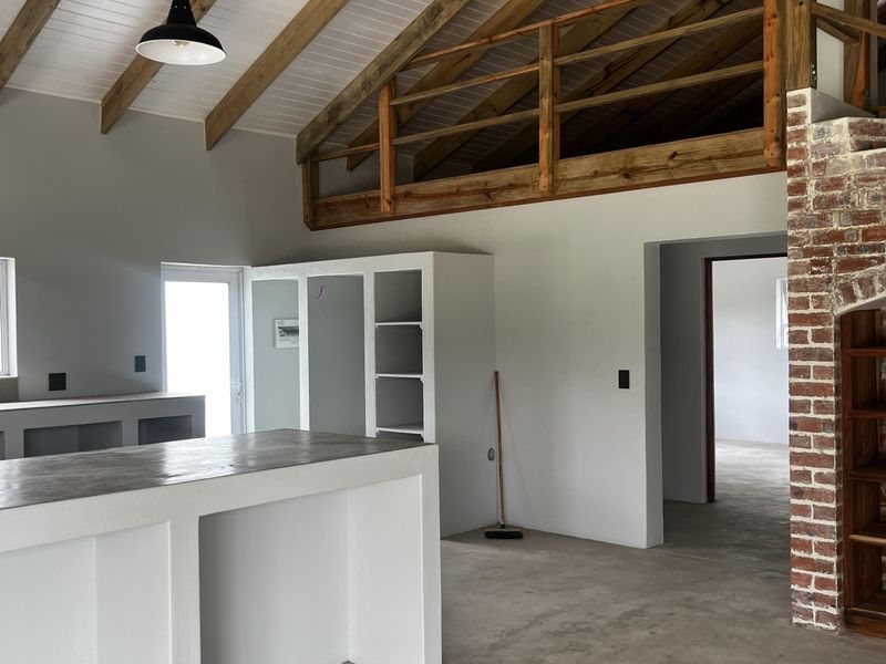 Spacious open-plan living area featuring exposed timber beams, a mezzanine loft, and a rustic brick fireplace, offering a versatile layout with concrete flooring.