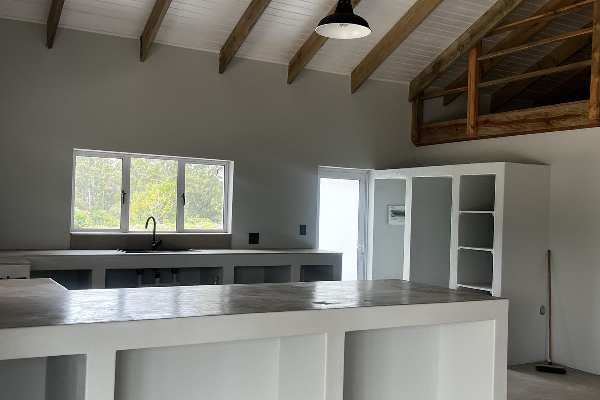 Spacious kitchen area featuring a vaulted ceiling with exposed timber rafters, a concrete island, and a mezzanine loft level, currently in an unfinished state.