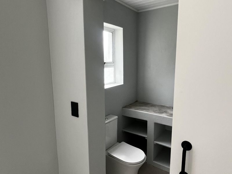 A clean, modern bathroom featuring a sliding barn door, built-in vanity storage, and a white toilet, finished with a tongue and groove ceiling.