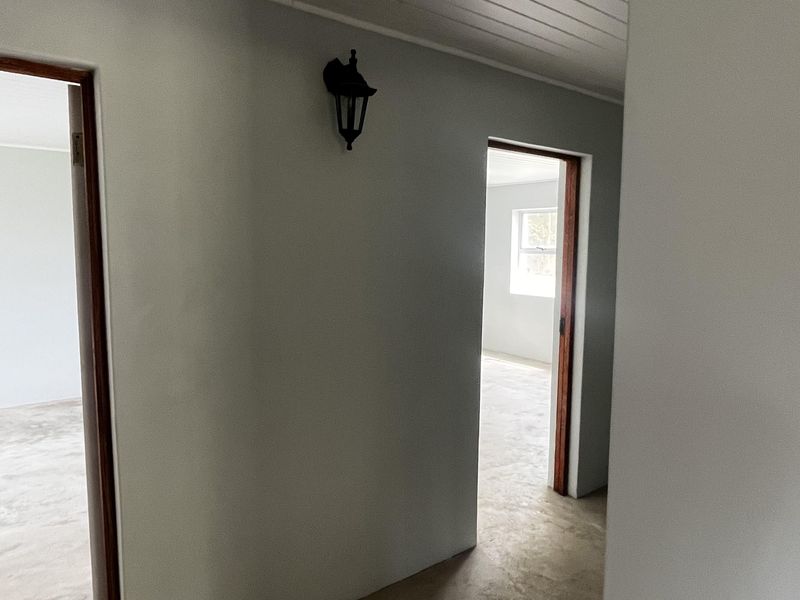 A clean, empty hallway featuring neutral walls, timber door frames, and a tongue and groove ceiling, providing access to adjacent rooms.