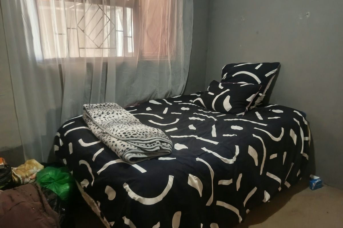 A bedroom featuring a window with security burglar bars and plain wall finishes.