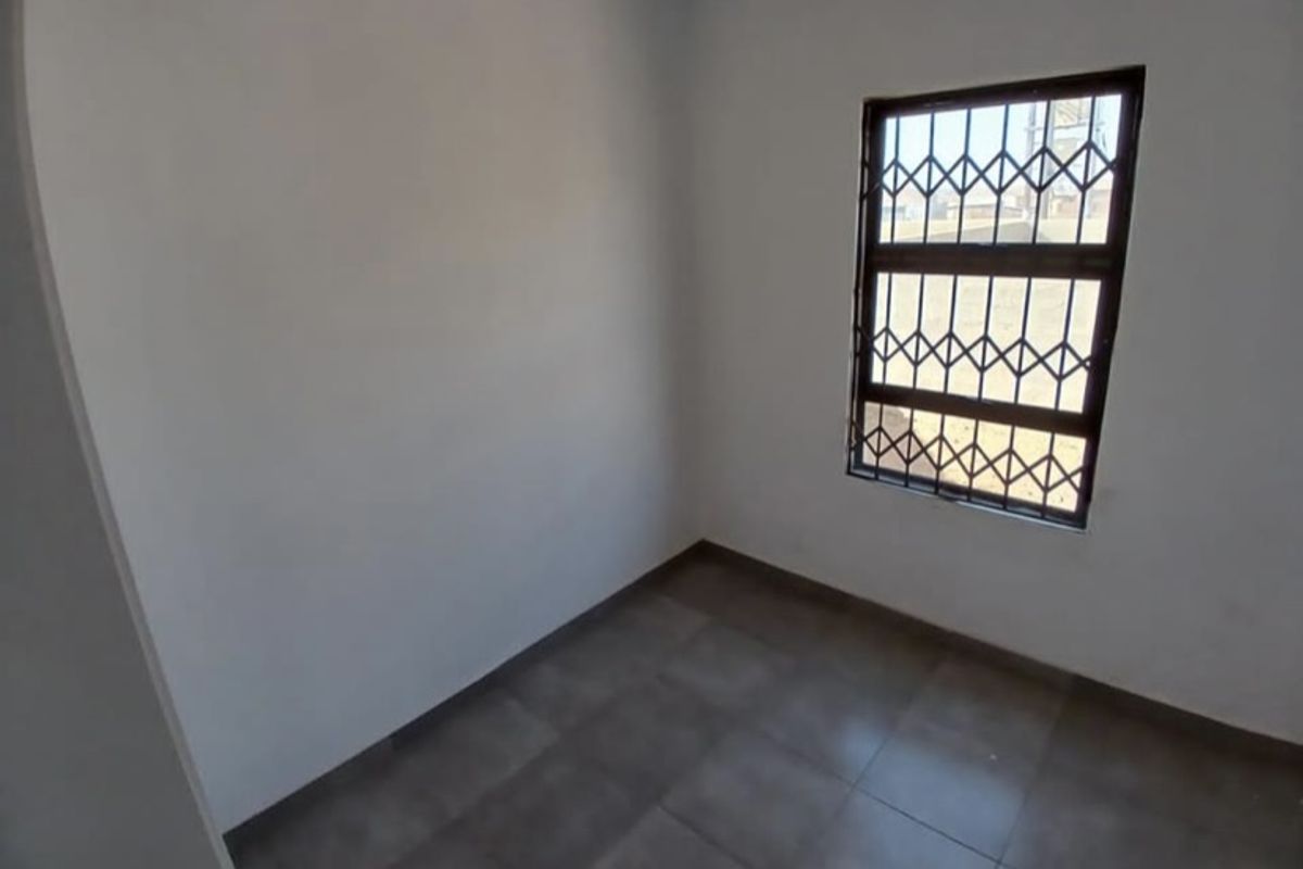 A clean, empty bedroom featuring neutral tiled flooring and a window fitted with a security gate.