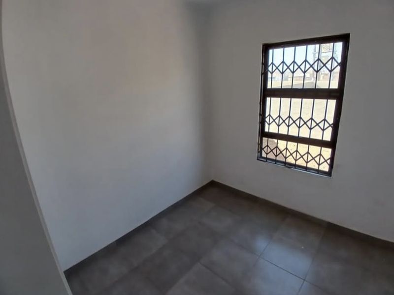A clean, empty bedroom featuring neutral tiled flooring and a window fitted with a security gate.