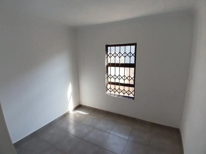 A clean, empty bedroom featuring neutral tiled flooring and a window fitted with a security gate.