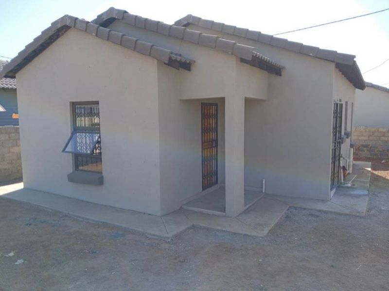 A neat, single-story residential house featuring a tiled roof, security gates, and a concrete apron surrounding the exterior.