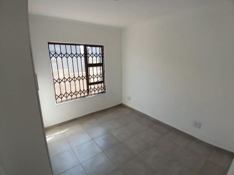 A clean, empty bedroom featuring neutral tiled flooring, white walls, and a window fitted with a security gate.