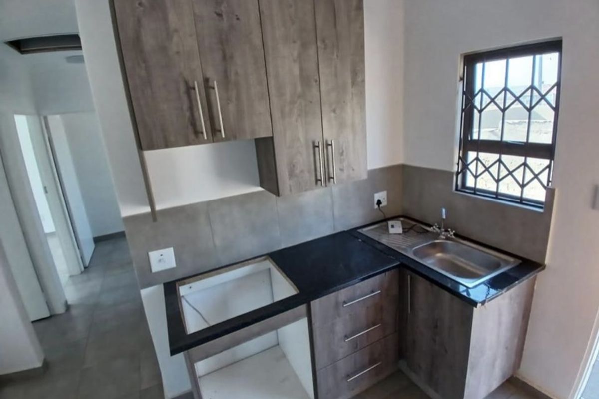 A compact kitchen featuring modern wood-look cabinetry, stone countertops, a stainless steel sink, and a tiled splashback, ready for appliance installation.