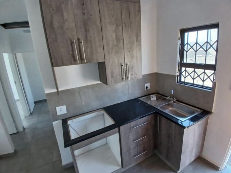 A compact kitchen featuring modern wood-look cabinetry, stone countertops, a stainless steel sink, and a tiled splashback, ready for appliance installation.