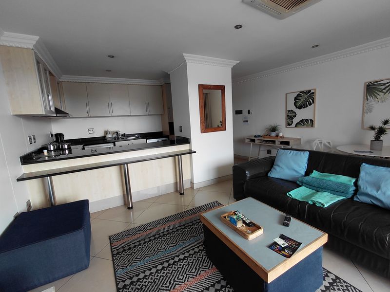 Open-plan living area featuring a modern kitchen with granite countertops, breakfast bar, and tiled flooring, seamlessly connected to the lounge space.