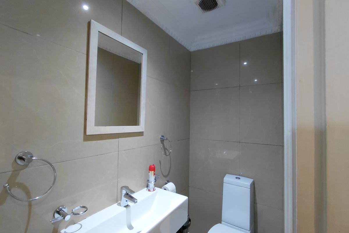 A compact bathroom featuring modern wall-mounted basin, toilet, and neutral wall tiling with an integrated extractor fan.