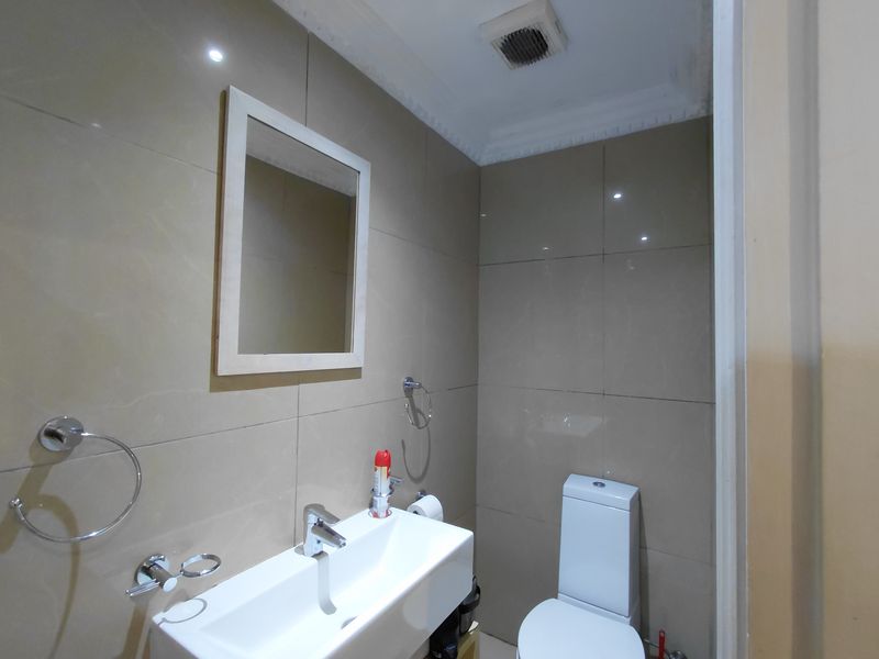 A compact bathroom featuring modern wall-mounted basin, toilet, and neutral wall tiling with an integrated extractor fan.
