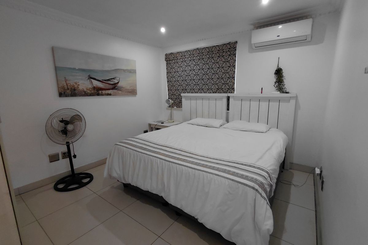 A well-maintained bedroom featuring tiled flooring, recessed ceiling lighting, crown molding, and a wall-mounted air conditioning unit.