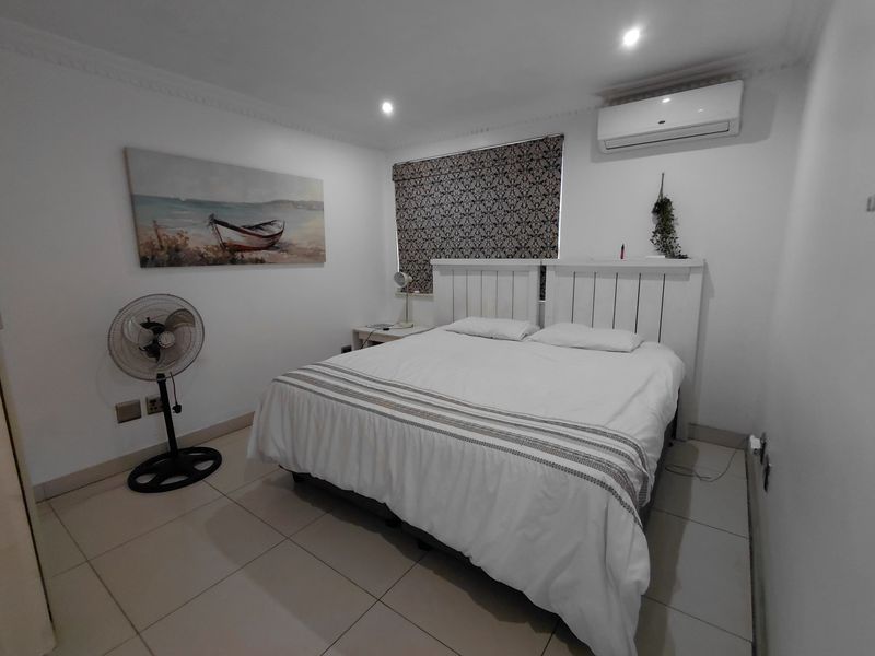 A well-maintained bedroom featuring tiled flooring, recessed ceiling lighting, crown molding, and a wall-mounted air conditioning unit.