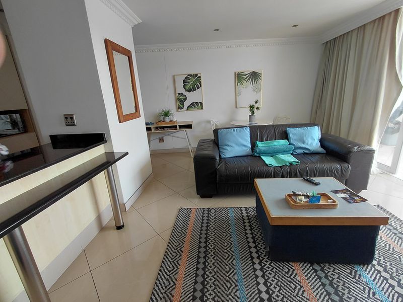 Open-plan living area featuring tiled floors, a breakfast bar with granite countertops, and direct access to a balcony through sliding glass doors.