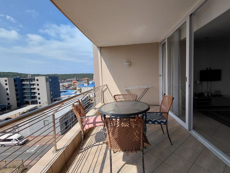 A covered balcony featuring tiled flooring and a stainless steel balustrade, offering an elevated view of the surrounding urban area.