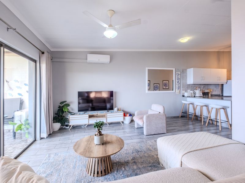 An open-plan living and kitchen area featuring tiled floors, a breakfast bar, split-system air conditioning, and direct access to an outdoor patio.