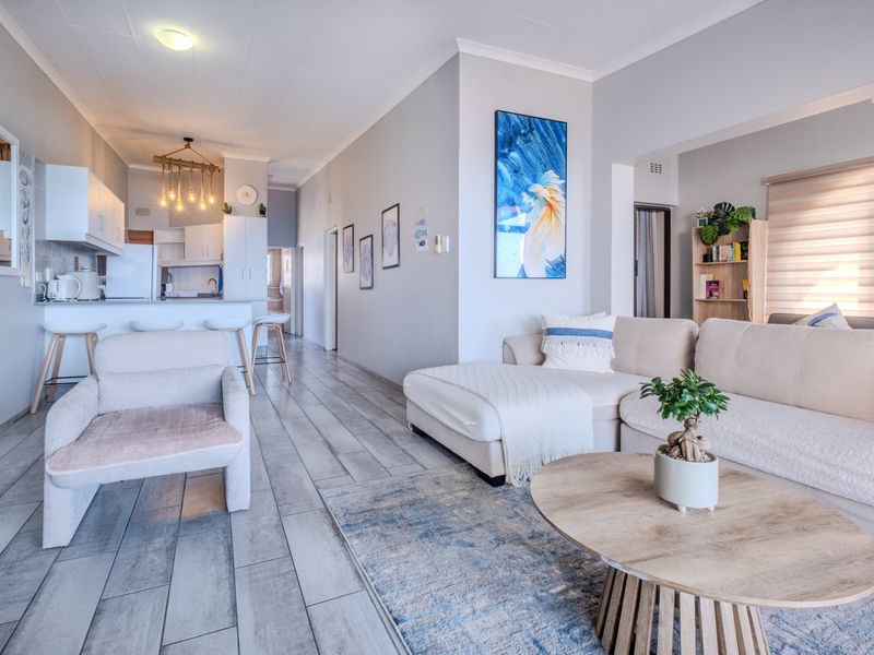 A bright open-plan living and kitchen area featuring modern tiled flooring, neutral wall tones, and a functional kitchen layout with a breakfast bar.