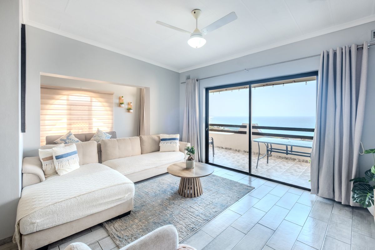 Bright and airy living room featuring tiled flooring, a ceiling fan, and large sliding glass doors that open onto a balcony with ocean views.