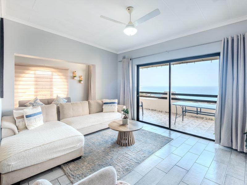 Bright and airy living room featuring tiled flooring, a ceiling fan, and large sliding glass doors that open onto a balcony with ocean views.