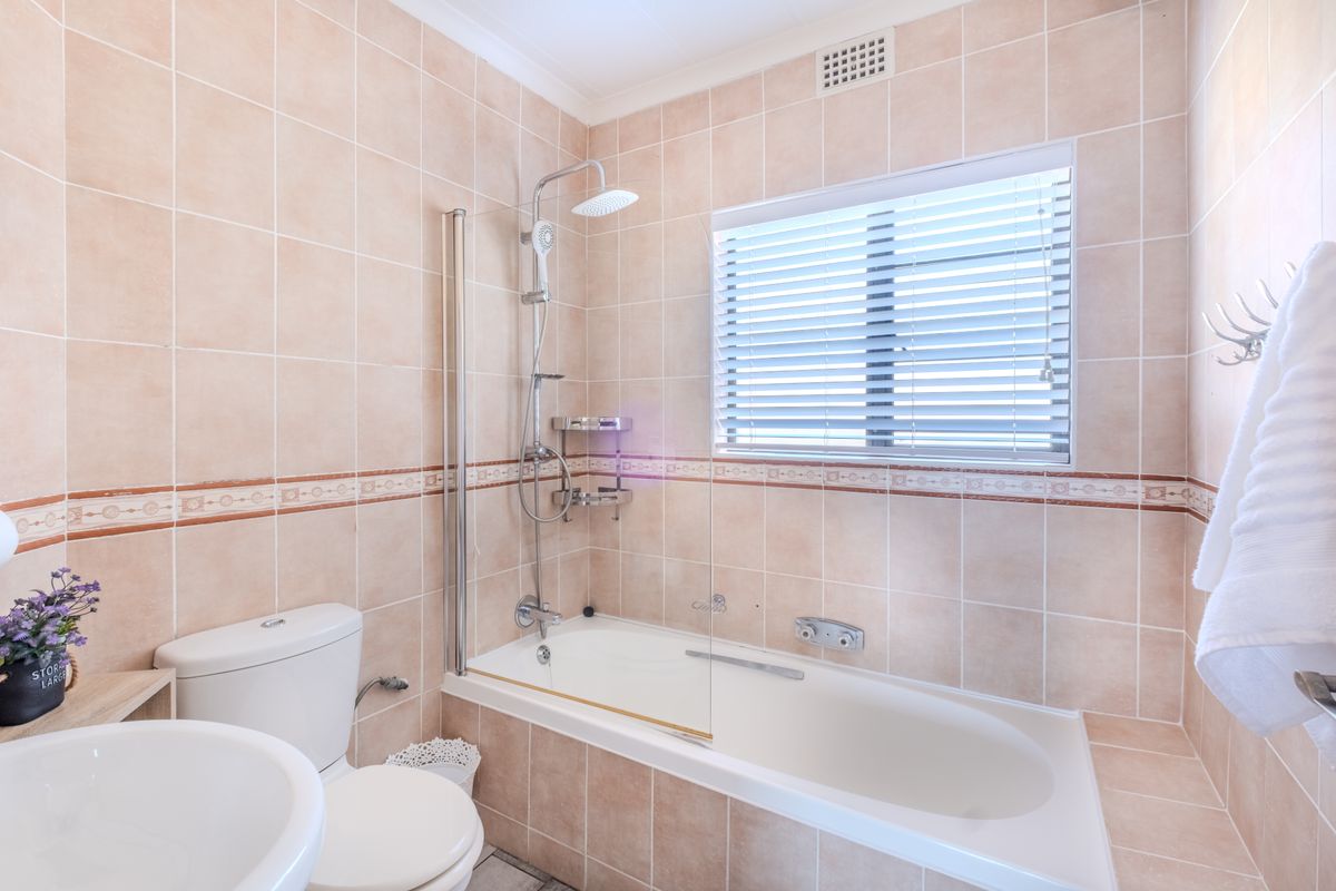 A functional bathroom featuring a built-in bathtub with shower, tiled walls, and a window for natural light and ventilation.