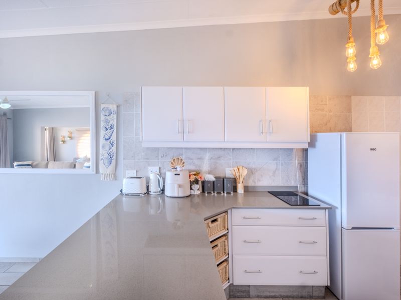 A clean and modern kitchen featuring stone countertops, white cabinetry, a tiled backsplash, and an integrated induction cooktop.