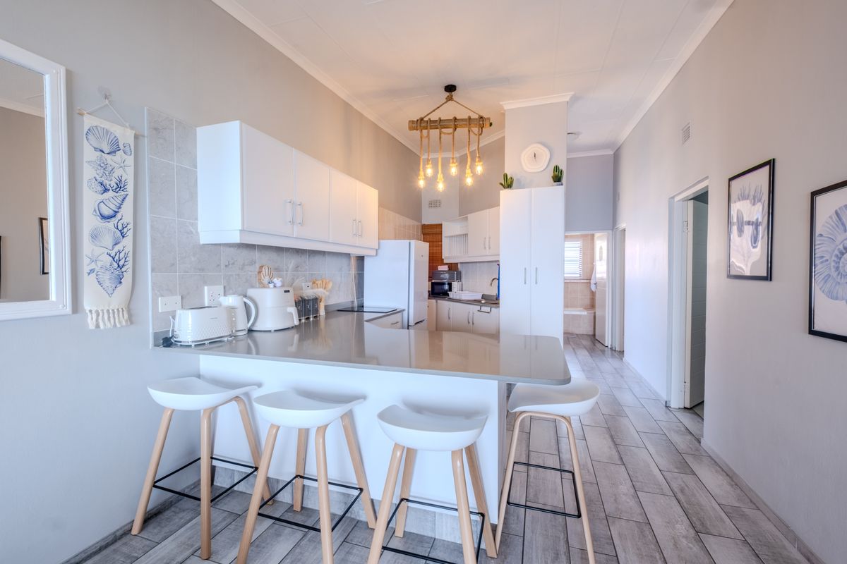 A modern, well-lit kitchen featuring white cabinetry, stone countertops, a tiled backsplash, and a breakfast bar with pendant lighting.