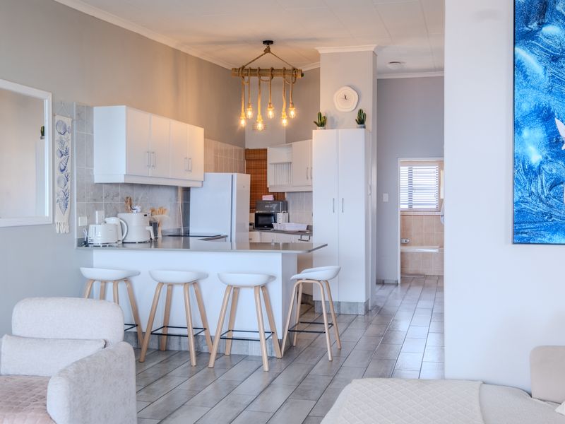 Open-plan living area featuring a functional kitchen with breakfast bar, tiled flooring, and modern cabinetry, seamlessly connecting to the adjacent living space.