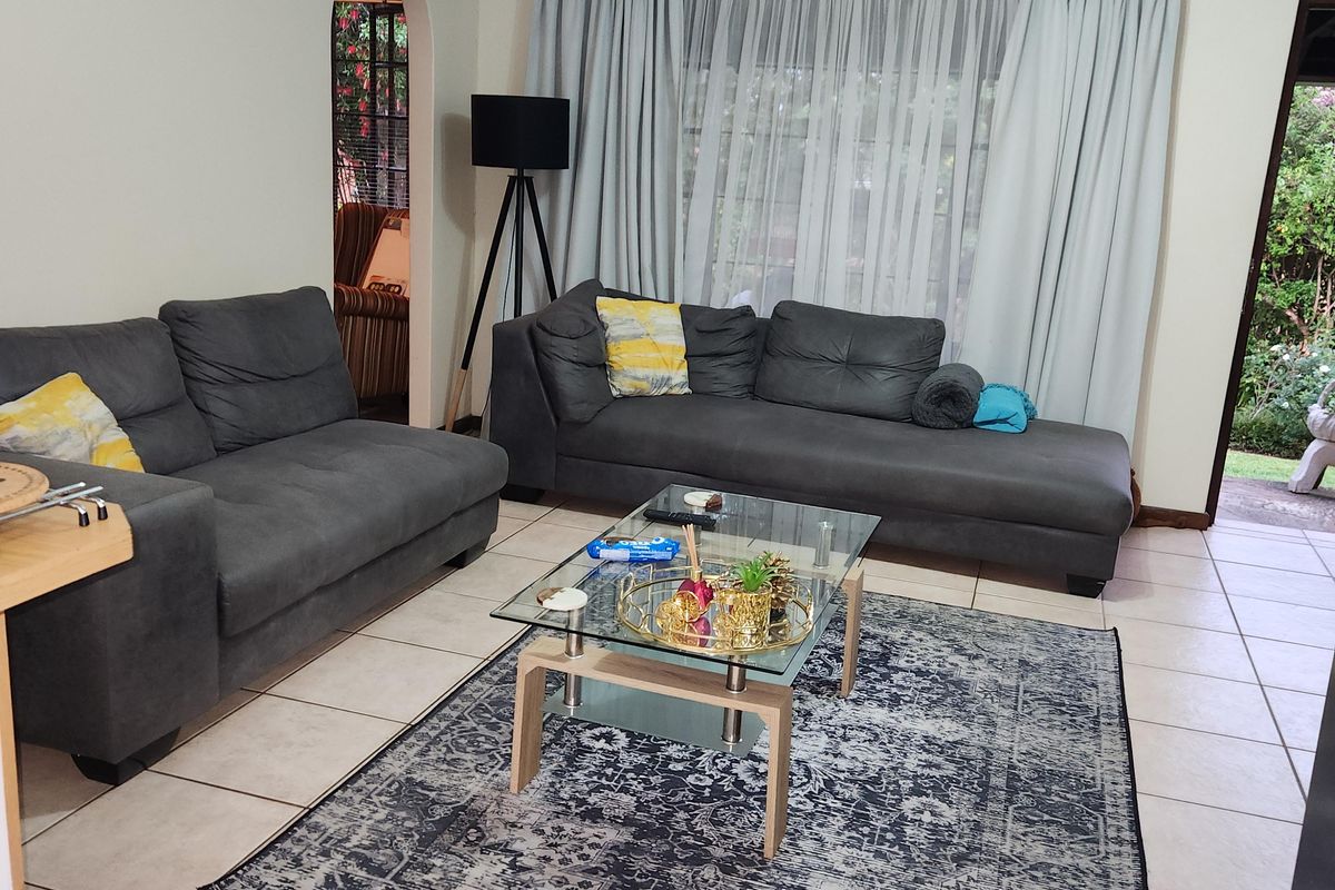 A spacious living room featuring neutral tiled flooring, an arched entryway, and large windows with curtains, providing a bright and functional living space.