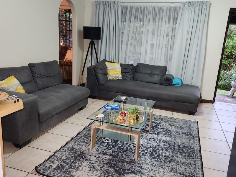 A spacious living room featuring neutral tiled flooring, an arched entryway, and large windows with curtains, providing a bright and functional living space.