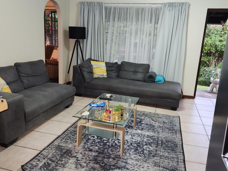 A spacious living room featuring neutral tiled flooring, an arched entryway, and direct access to the garden area through a doorway.