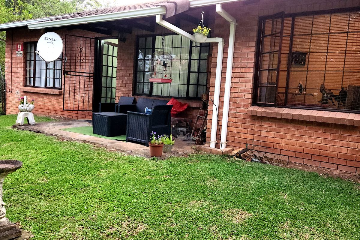 Rear view of a brick townhouse featuring a concrete patio area, security bars on windows, and a well-maintained lawn.