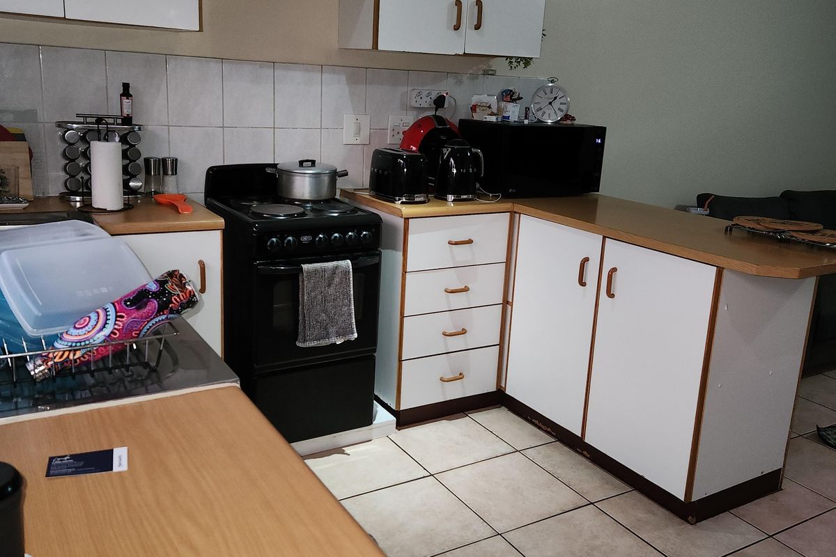 A functional kitchen featuring white cabinetry, laminate countertops, tiled backsplash, and ceramic floor tiles, offering a practical layout for daily meal preparation.