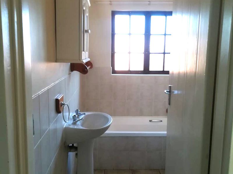 A functional bathroom featuring a pedestal basin, bathtub, tiled finishes, and a wall-mounted medicine cabinet, offering a clean and simple layout.
