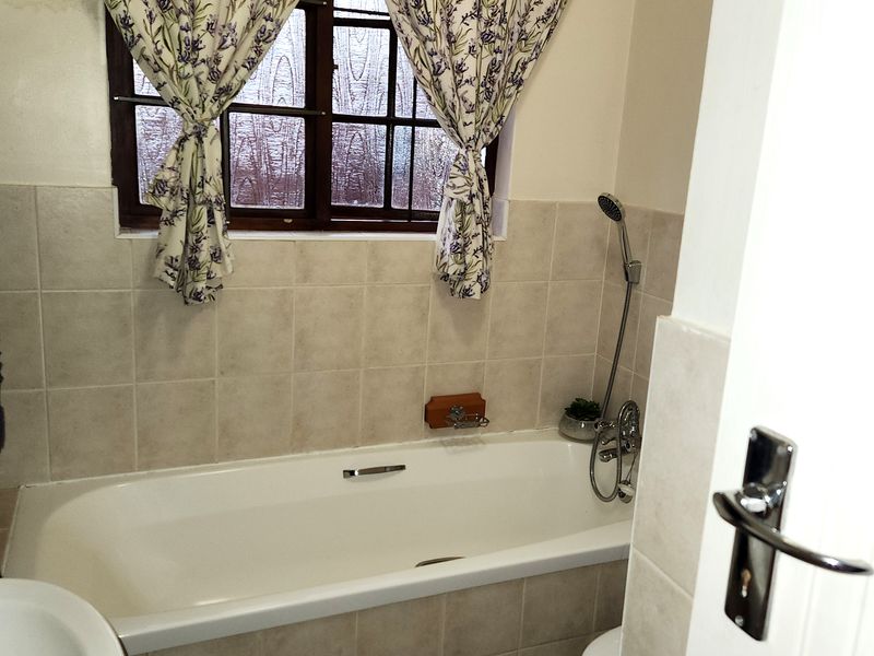 A functional bathroom featuring a bathtub with a handheld shower attachment, tiled walls, and a window, offering a standard layout for a townhouse.