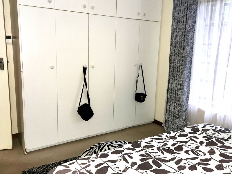 A bedroom featuring floor-to-ceiling built-in cupboards with white cabinetry and a window with curtain fixtures.