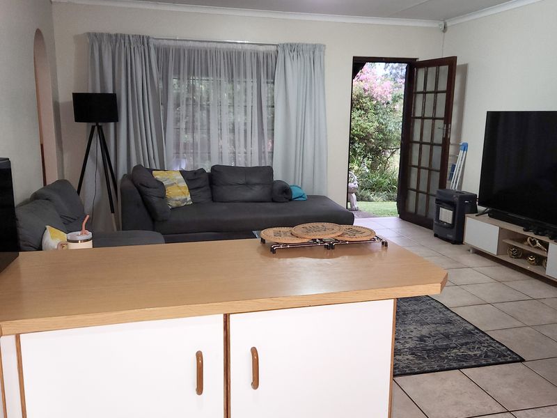 Open plan living area featuring tiled flooring, a kitchen island with cabinetry, and direct access to the garden through a glass-paneled door.