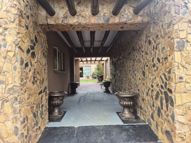 A covered outdoor patio area featuring rustic stone-clad walls and exposed timber beam ceilings, leading to a paved garden courtyard.
