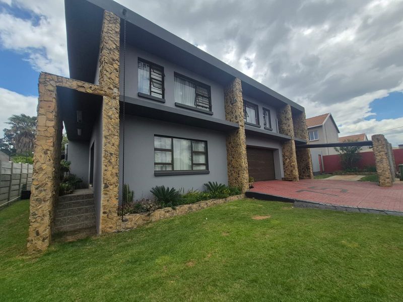 Modern double-storey home featuring striking stone cladding, a paved driveway, double garage, and well-maintained front garden.