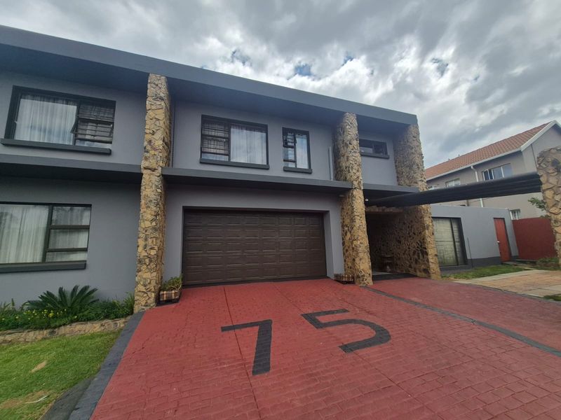 Modern double-storey residential facade featuring stone-clad pillars, a paved driveway with integrated house number, and a secure double garage.